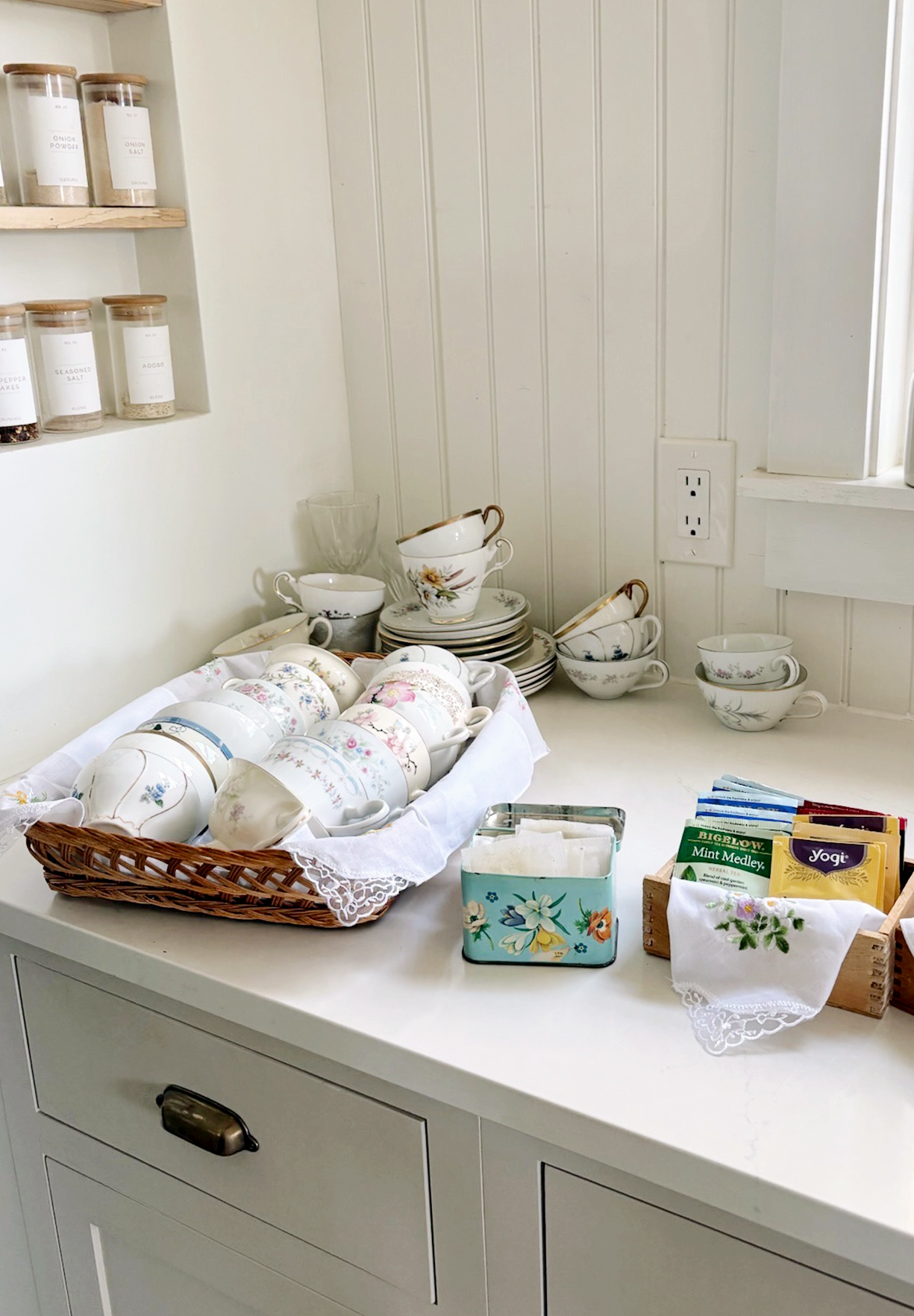 basket filled with vintage tea cups next to tin of tea and extra tea cups stacked behind it